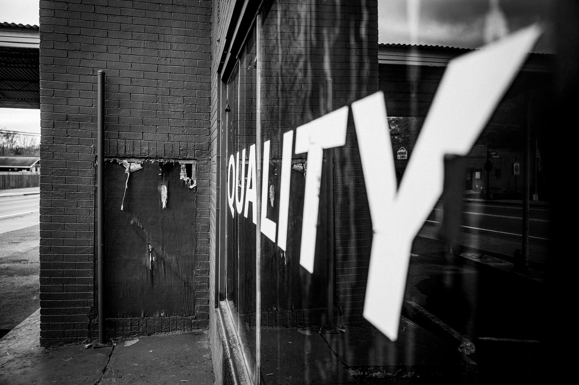 A black and white photo showcasing reflection and urban street art with 'QUALITY' text visible.
