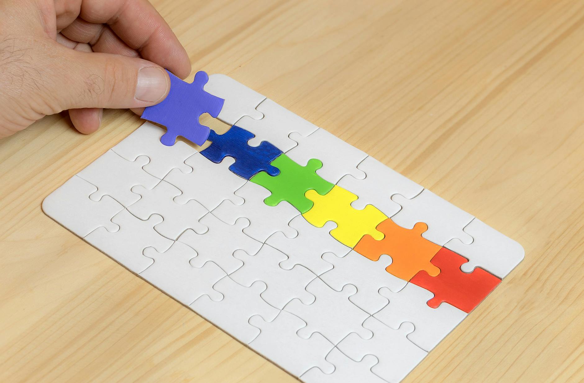 A hand places the final piece in a colorful rainbow puzzle with wooden background.