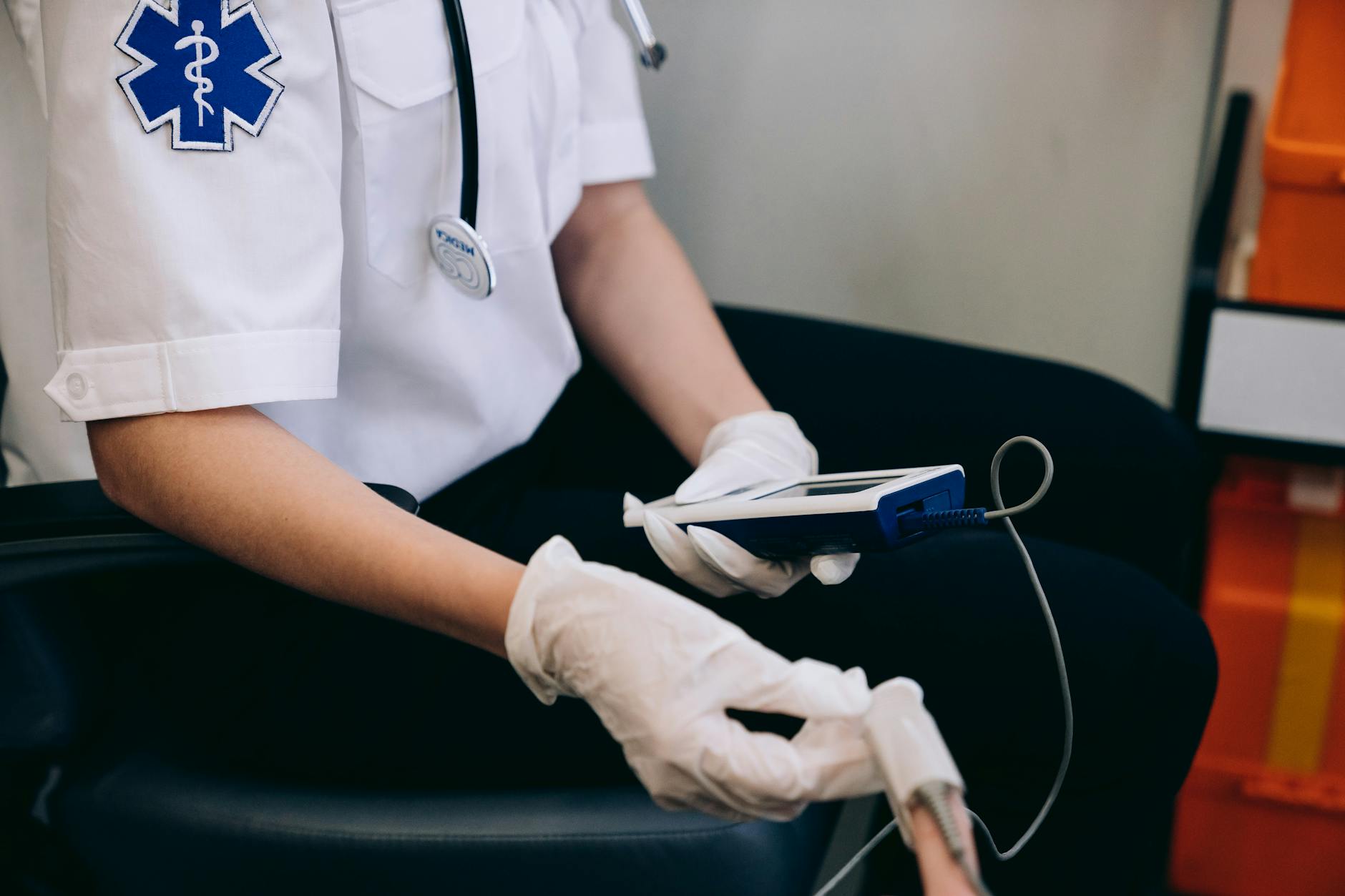 A paramedic monitors patient vitals using handheld medical equipment indoors.