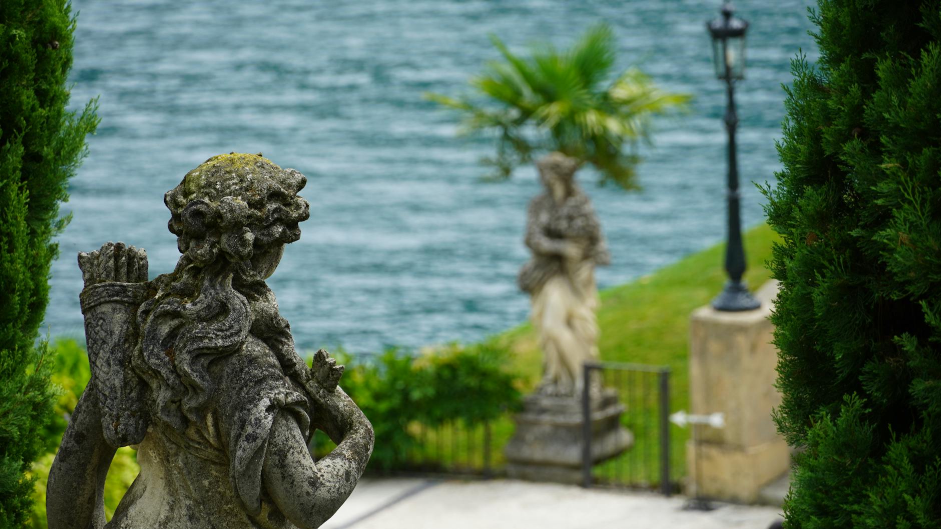A serene view of ancient statues and lush greenery by Lake Como, Italy.