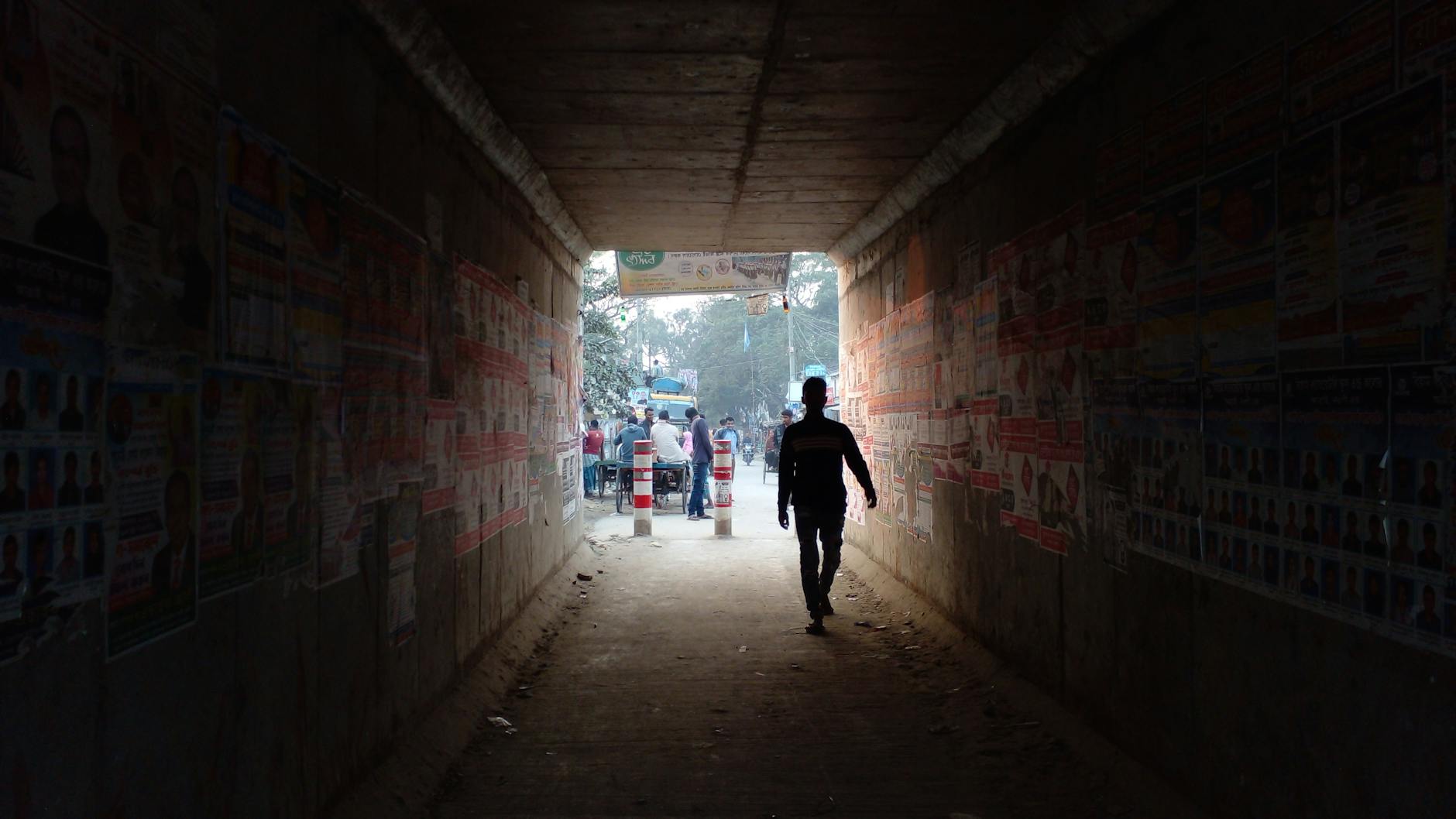 A silhouette of a man walking through a tunnel in Atrai, Bangladesh showcasing urban life.