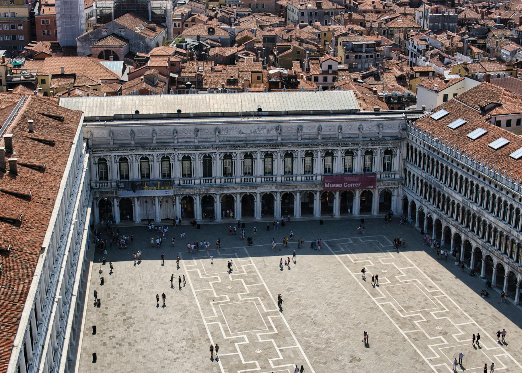Aerial shot of Venice's Museo Correr and St. Mark's Square with historic architecture and scattered crowds.