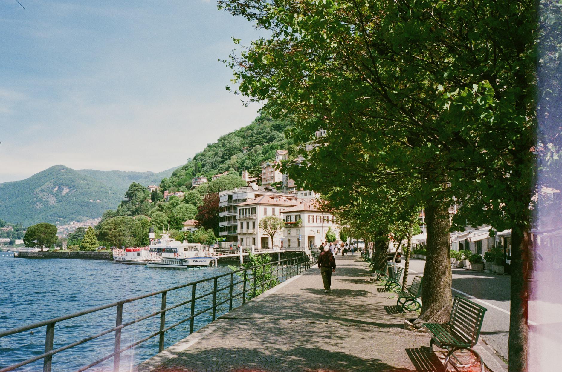 Beautiful lakeside promenade in Como, Lombardy, Italy with lush greenery and clear blue skies.