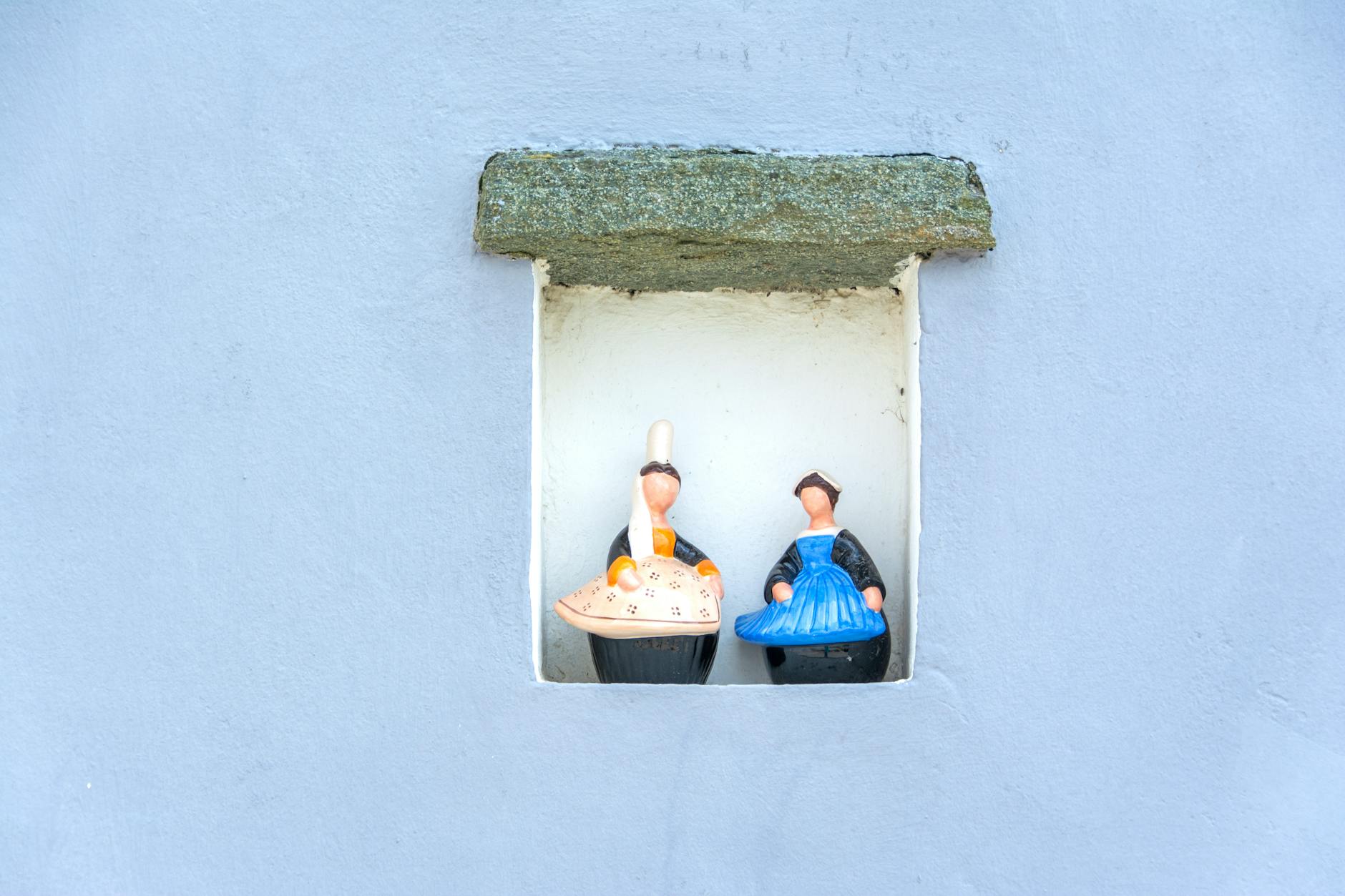 Charming porcelain figurines displayed in a niche with a serene blue wall background.