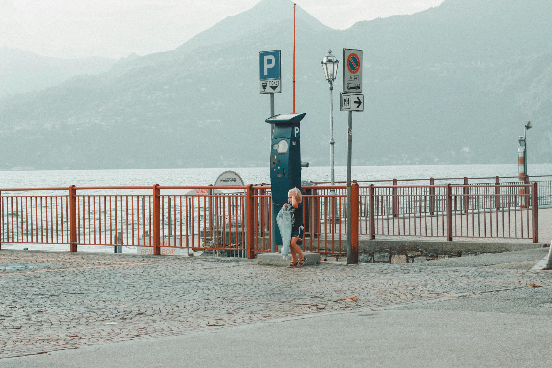 Child standing by parking area with mountains and lake view in Como, Italy.