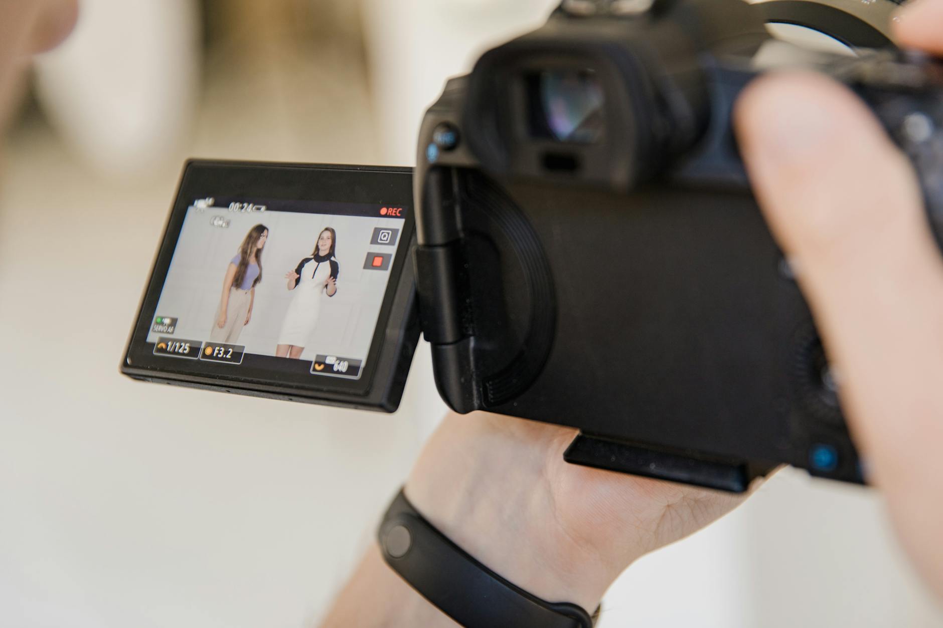 Close-up of a digital camera screen capturing two women recording content indoors.