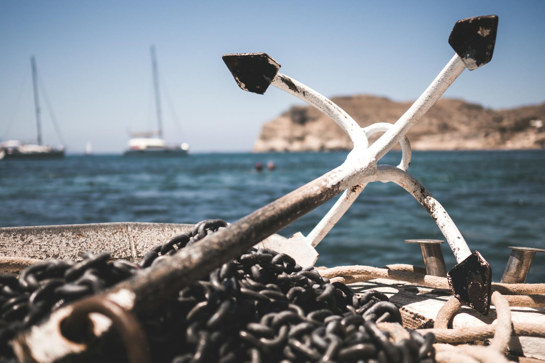 Close-up of boat anchor and chains with ocean and sailboats in the background.