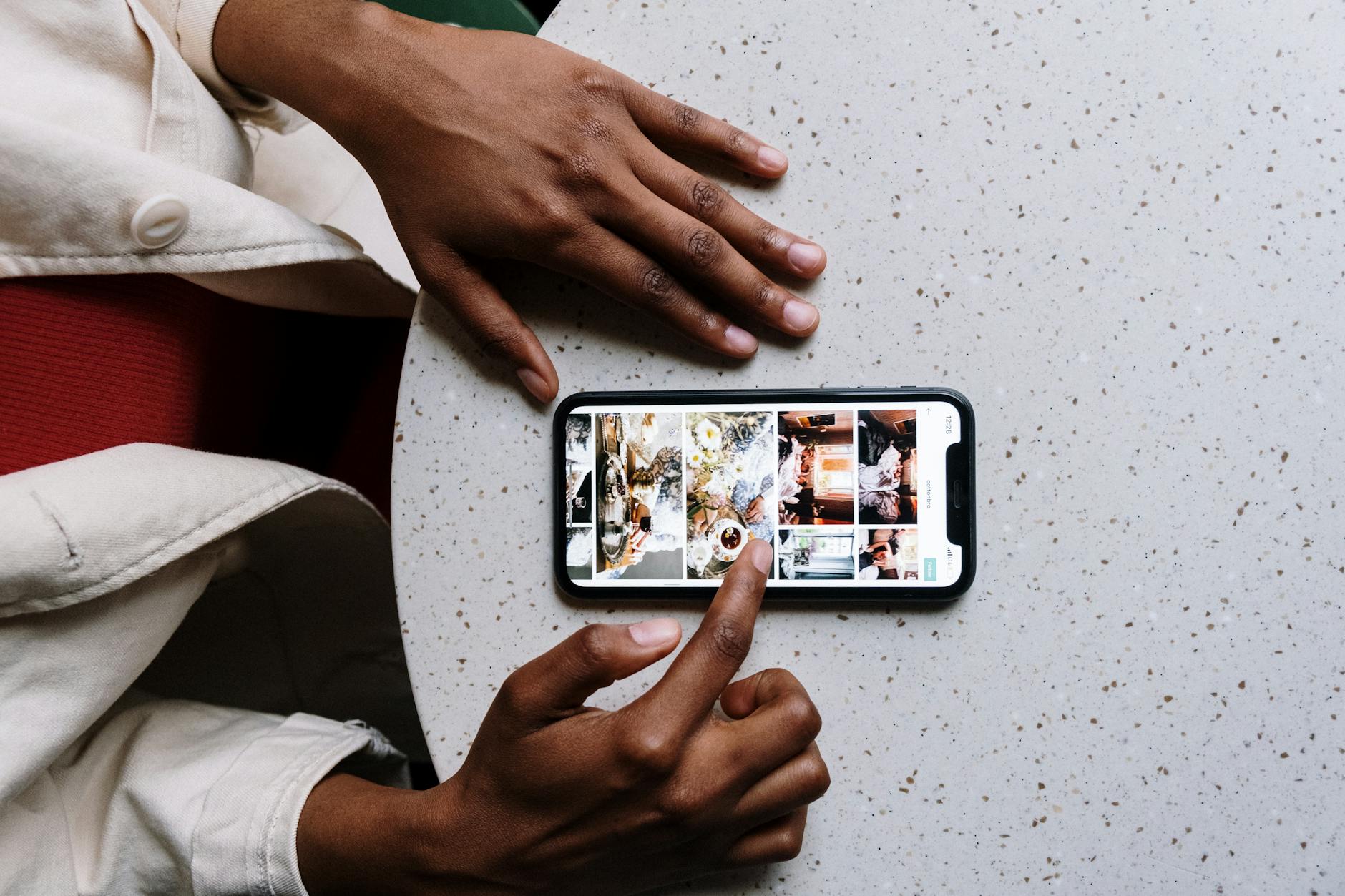 Close-up of hands using a smartphone on a cafe table, browsing social media or photos.
