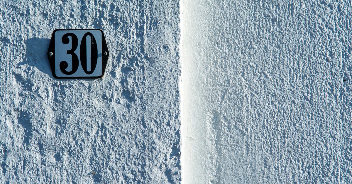 Close-up of a textured white wall featuring a classic house number 30 sign.