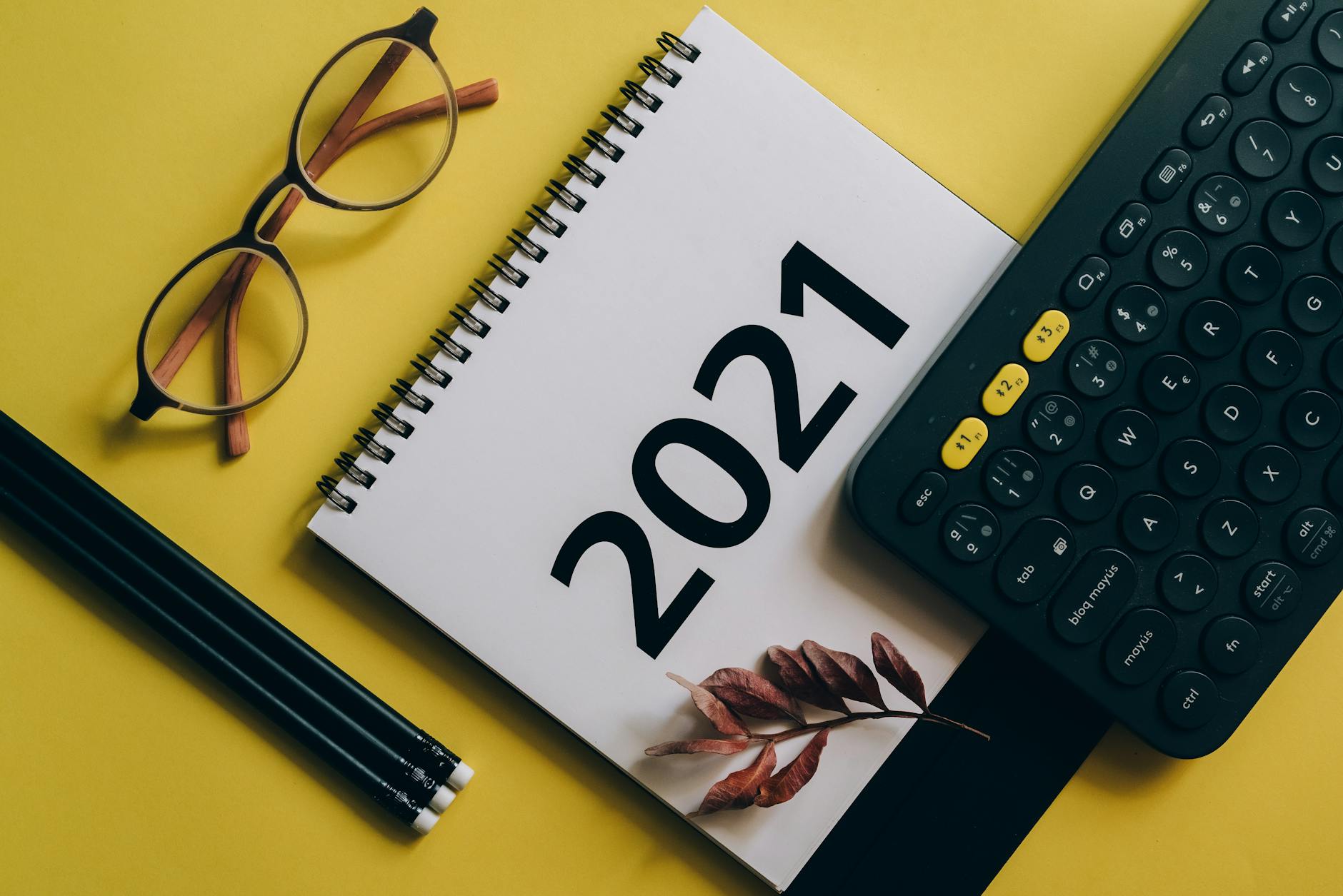 Flat lay of 2021 calendar, keyboard, and eyeglasses on yellow background.