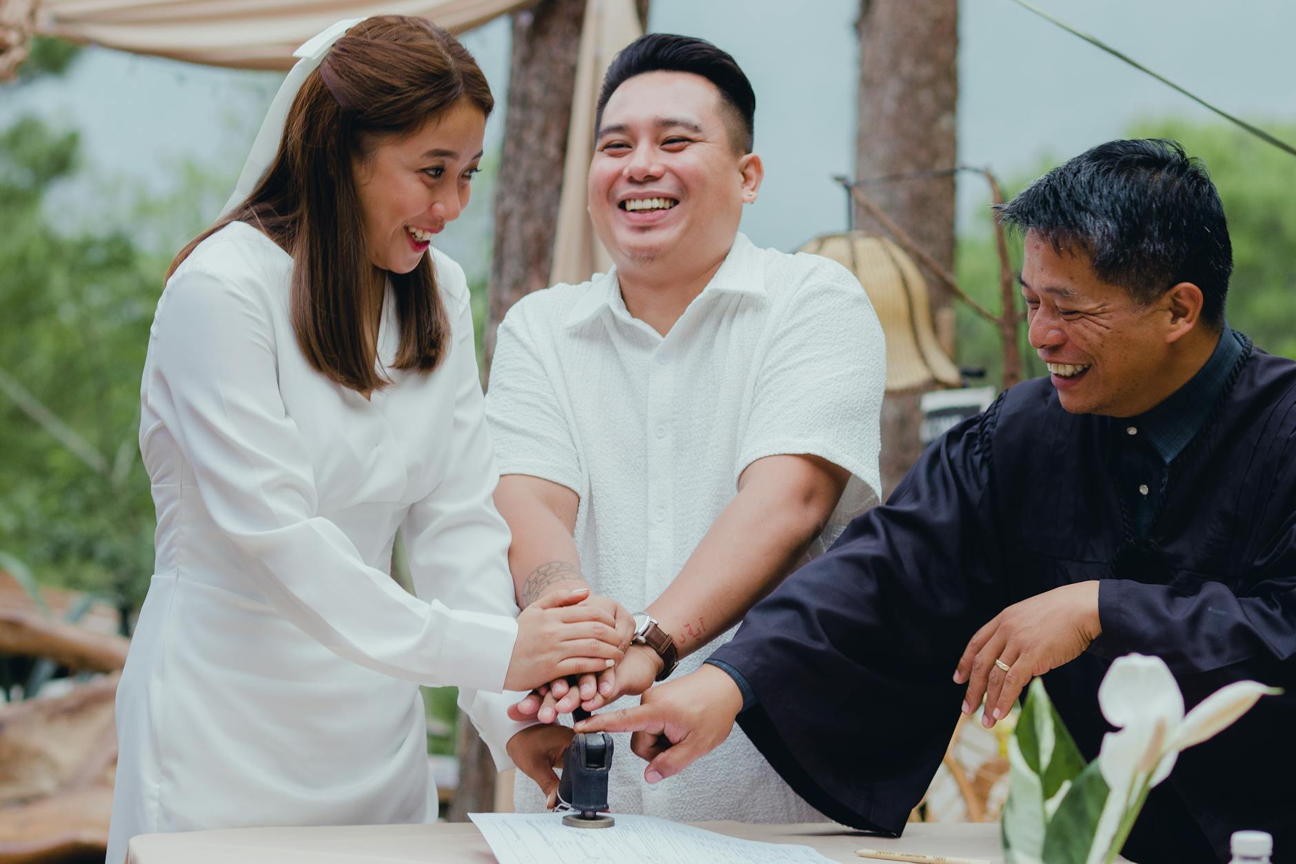 Happy couple with registrar stamping wedding document outdoors, celebrating marriage.