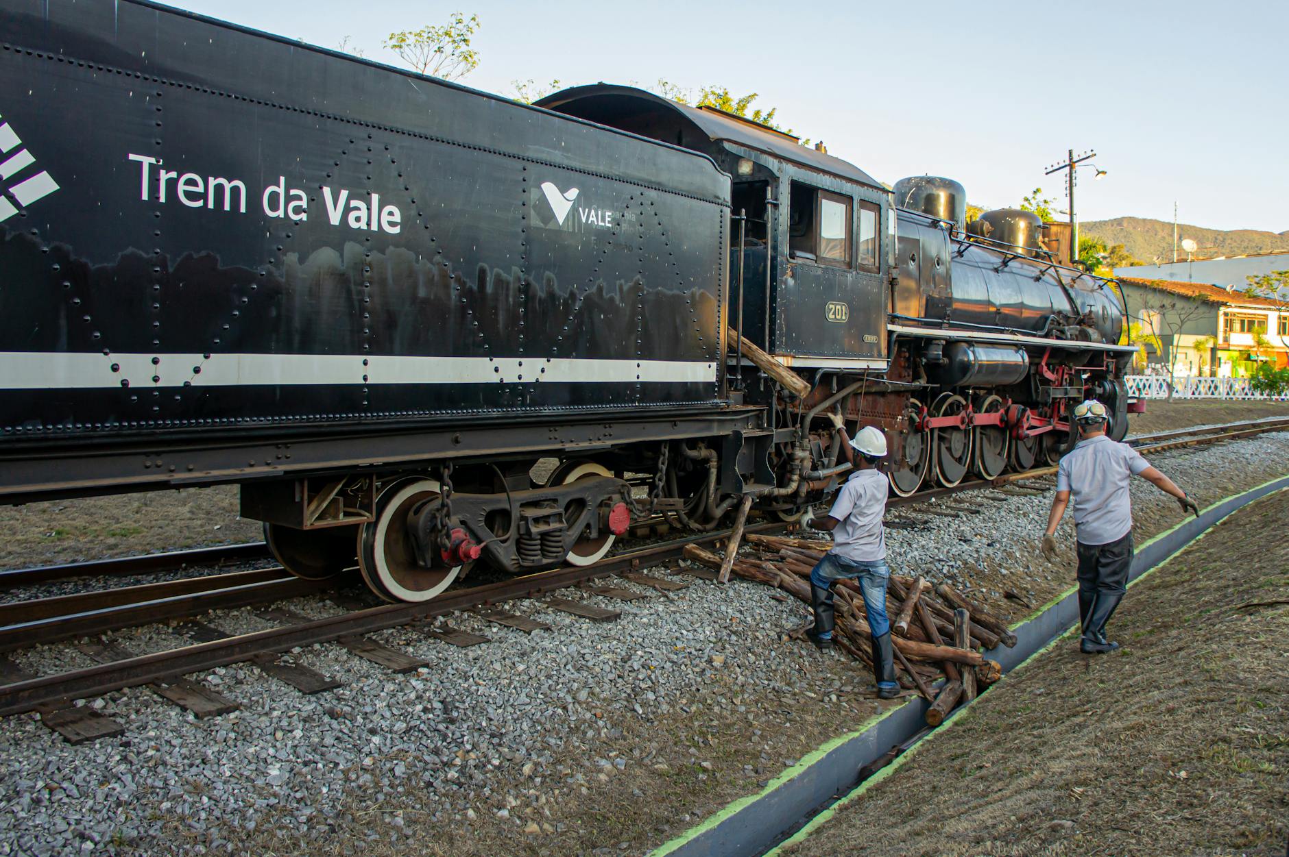 Men working on a Trem da Vale locomotive with wooden supplies on the tracks.