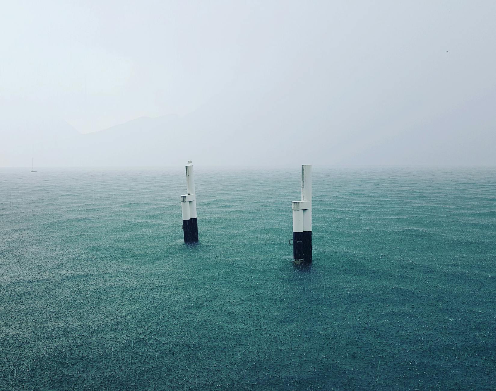 Moody seascape of Lake Como with rain falling on calm waters and visible buoys.