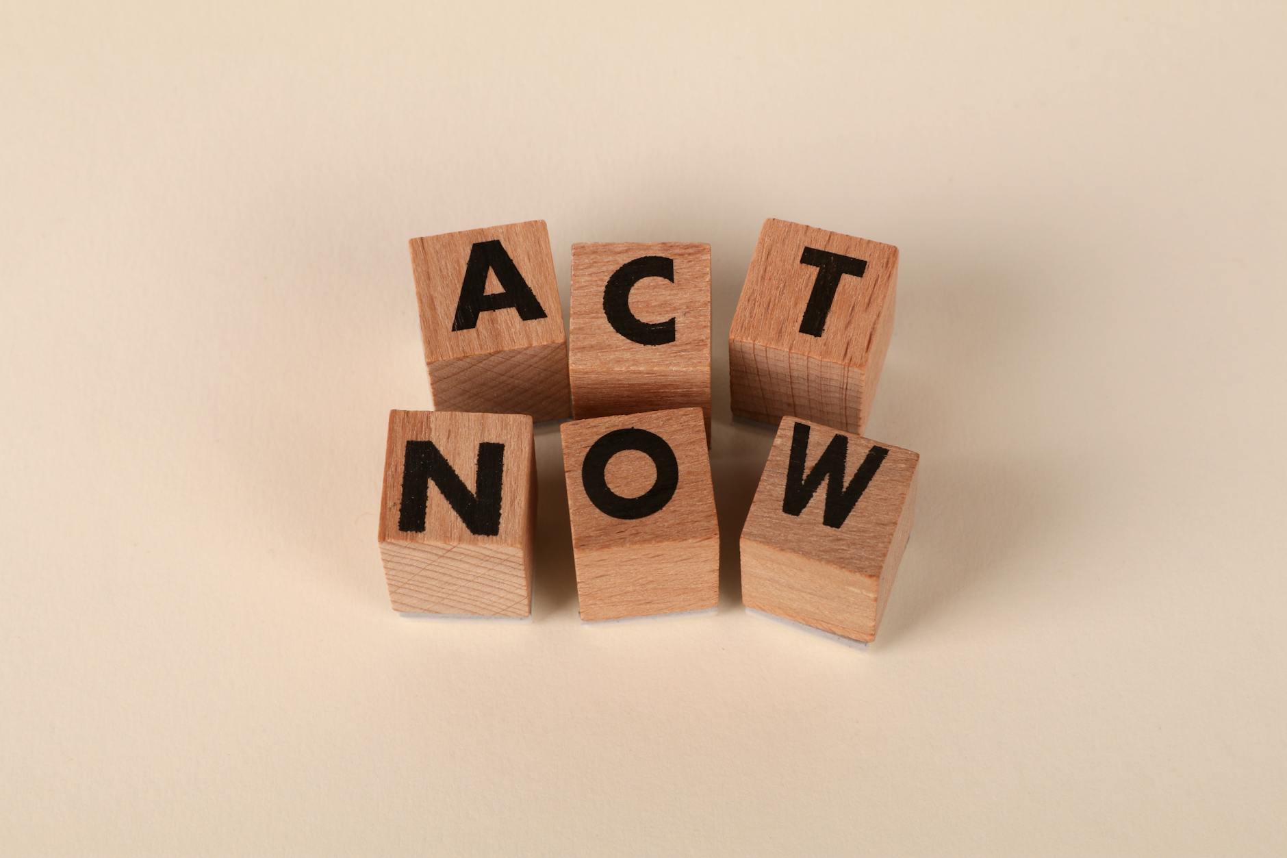 Wooden blocks with letters spelling 'ACT NOW', promoting urgency and motivation.