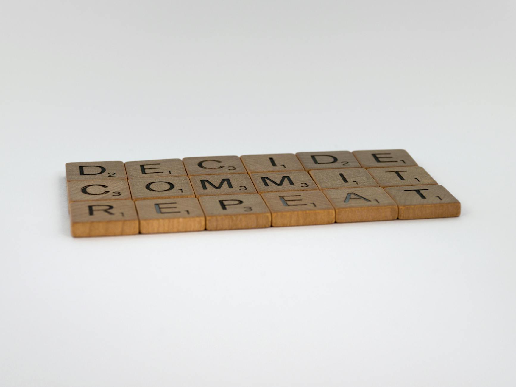 Wooden tiles arranged to spell 'DECIDE COMMIT REPEAT' on a white background.