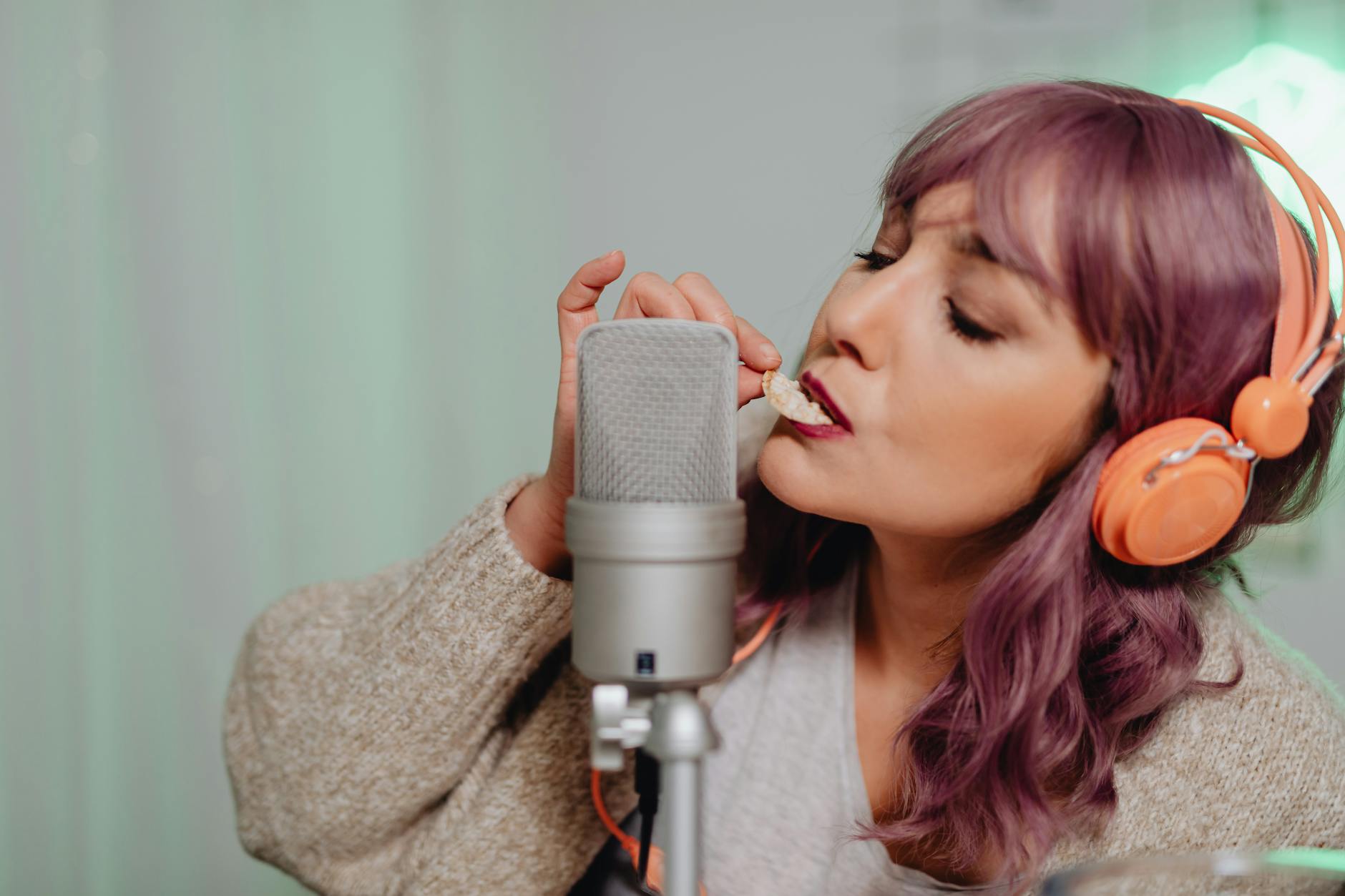 Young woman recording ASMR content with a microphone and headphones indoors.