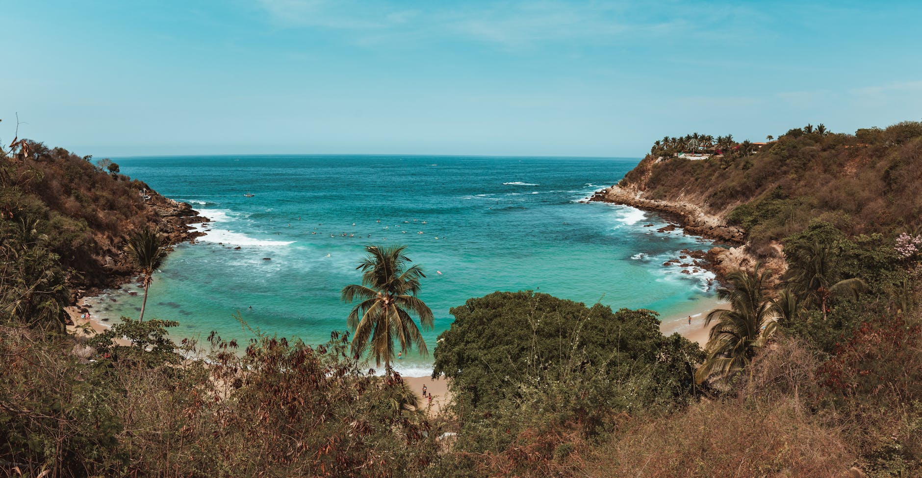 A beautiful seaside view of a secluded cove in Puerto Escondido, Mexico with clear blue waters and lush greenery.