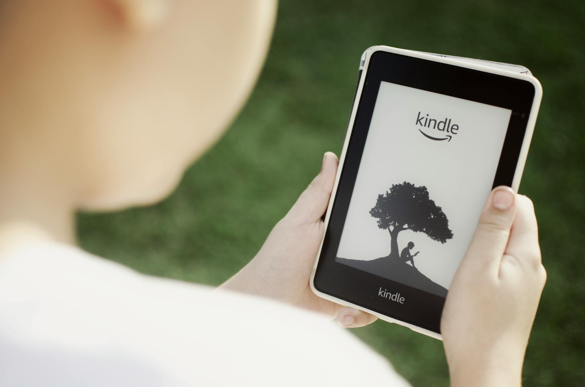 A child holds a Kindle device outdoors, highlighting the ease of reading with technology.