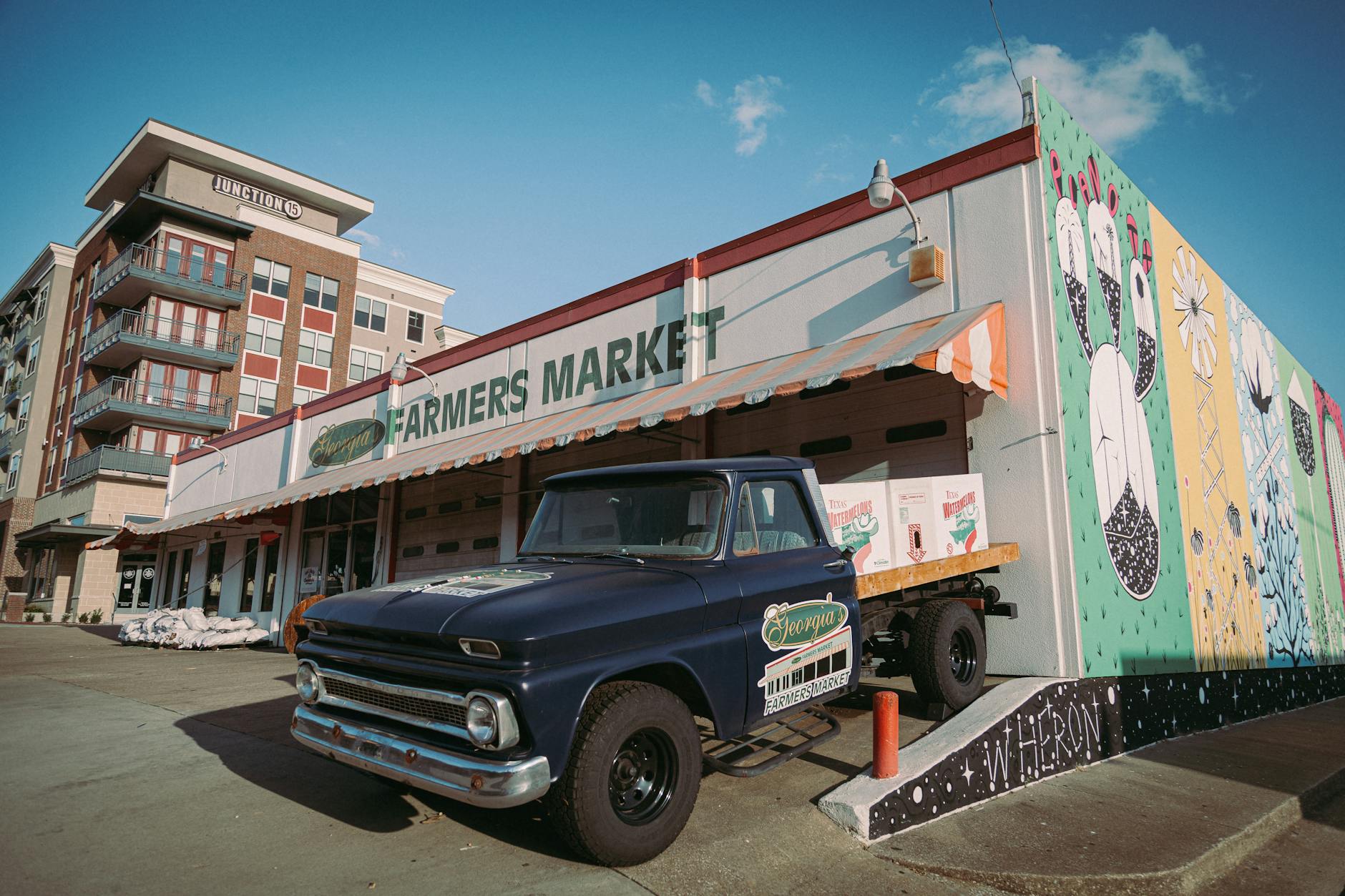 A classic truck parked outside a colorful farmers market in Plano, Texas, under a clear sky.