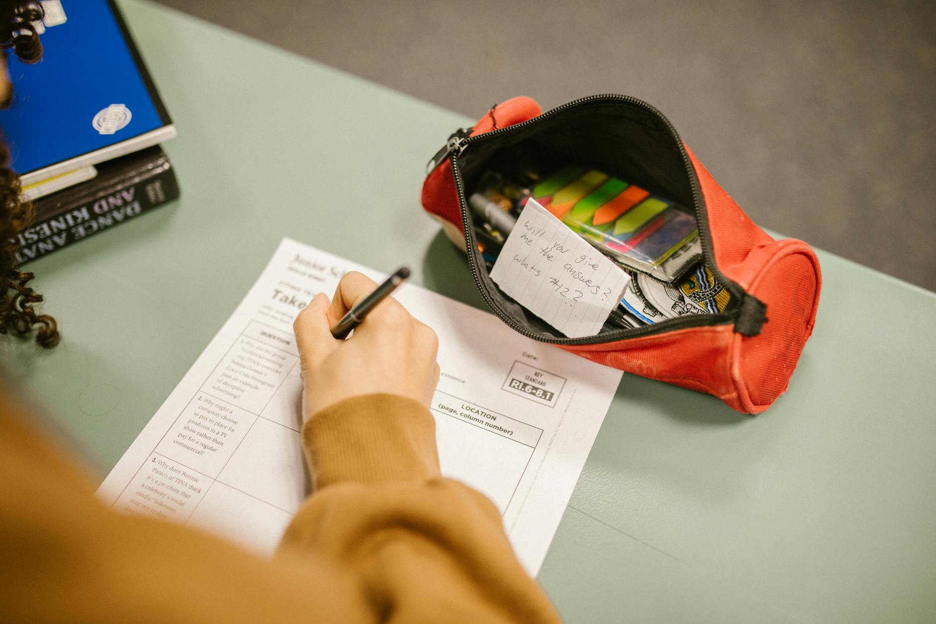A college student using cheat notes during an exam with visible test paper and pencil case.