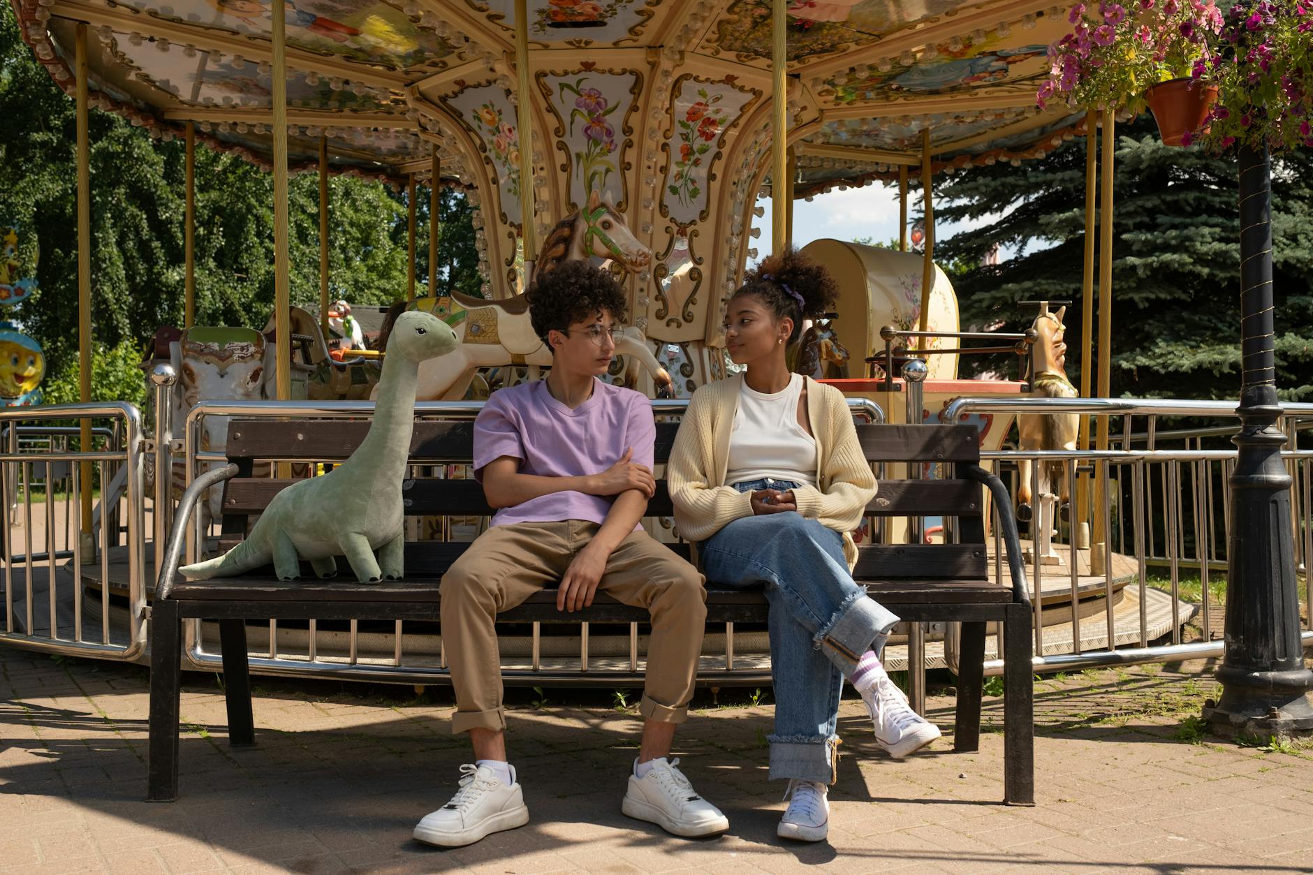 A couple enjoys a relaxing moment on a bench in front of a carousel at an amusement park.
