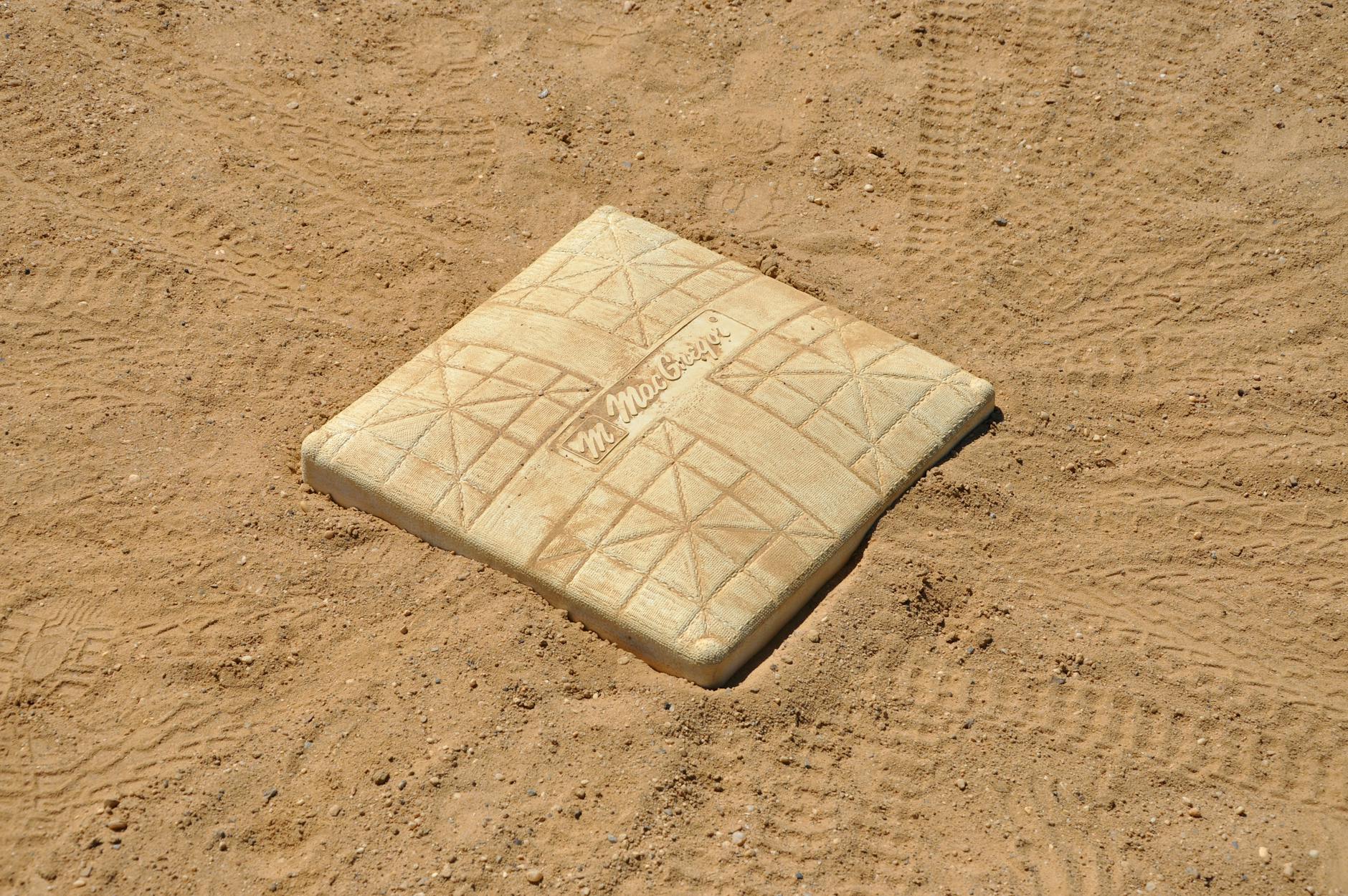 A detailed close-up of a baseball base on a dirt field, showing tire tracks.