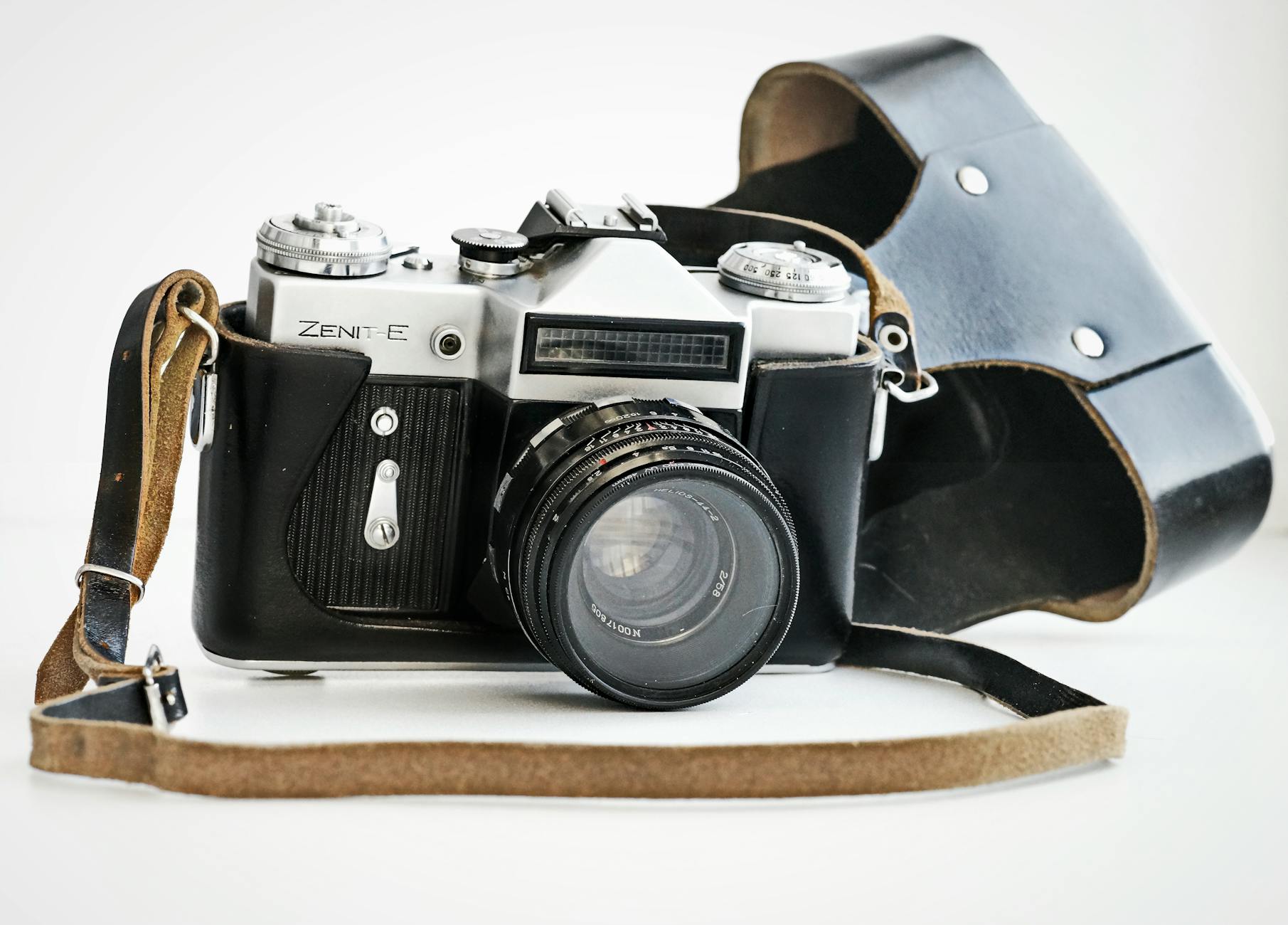 A detailed shot of a Zenit-E vintage film camera with its leather case on a white surface.