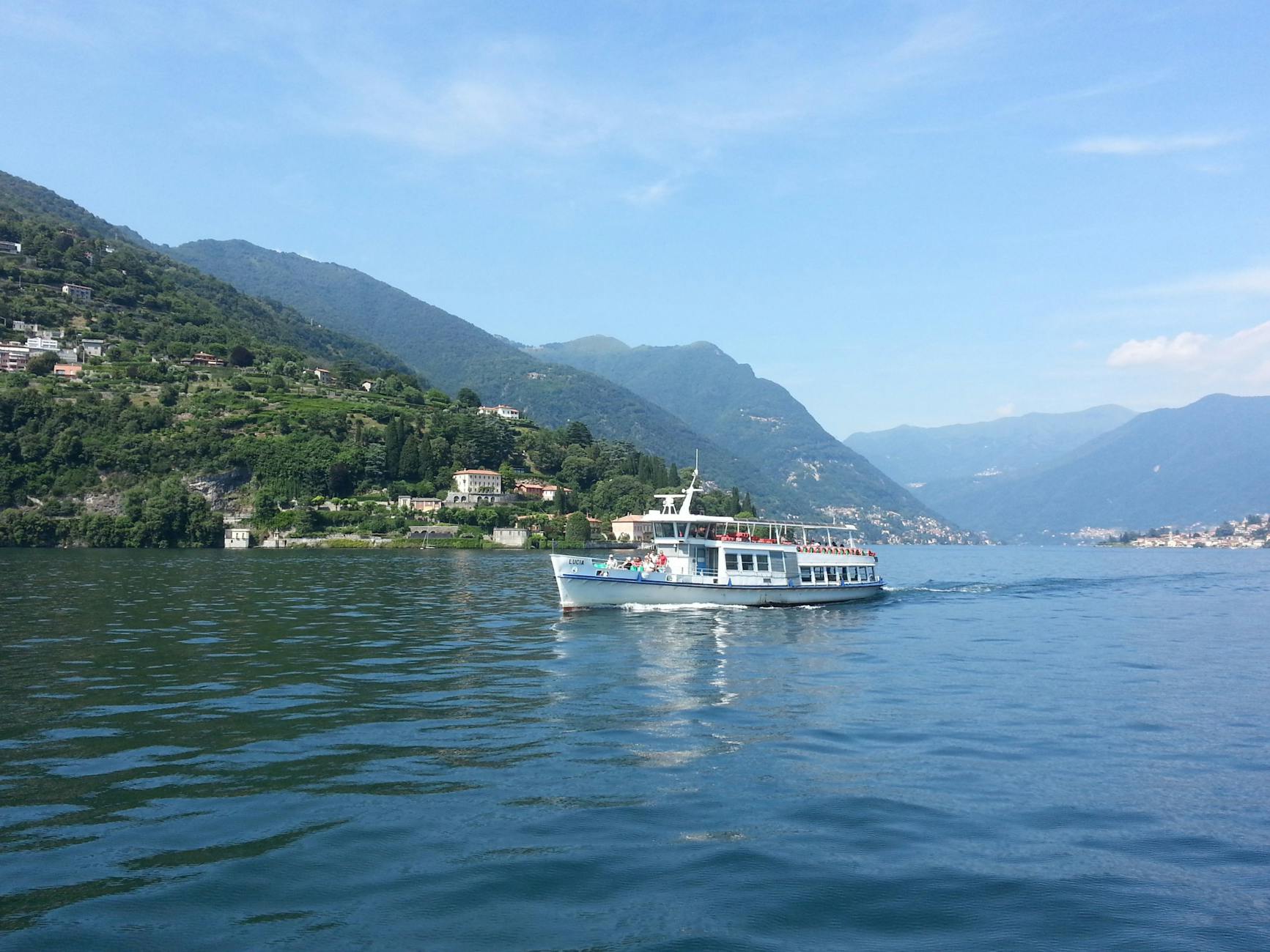 A ferry cruises on the picturesque Lake Como, surrounded by lush hills in Lombardy, Italy.