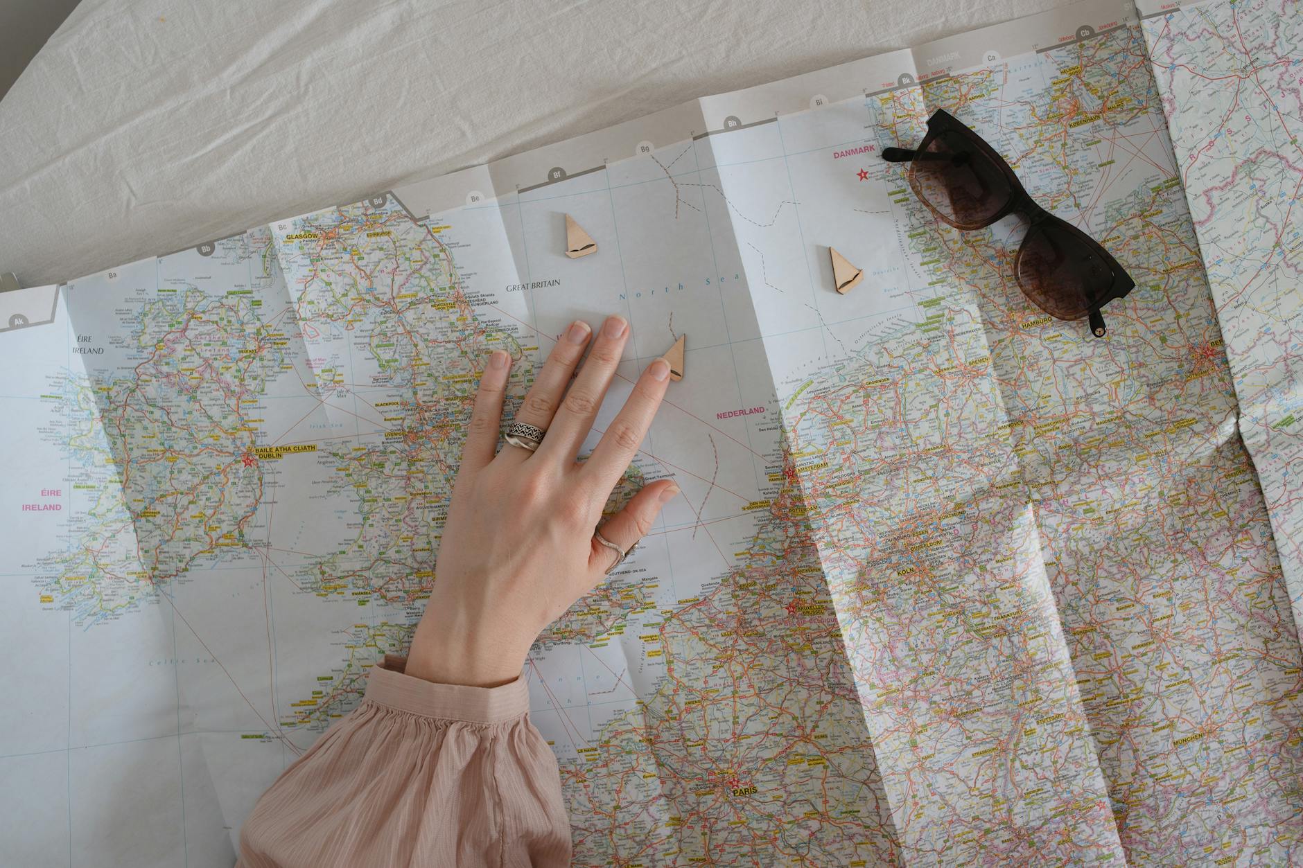 A hand exploring a map with sunglasses for travel planning.