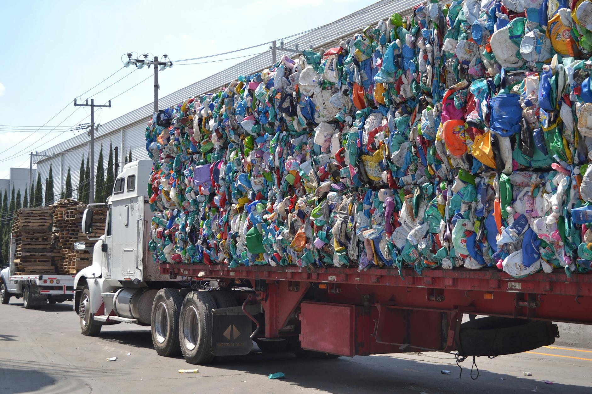 A large truck carrying bales of compressed plastic waste on a sunny city street in Mexico.