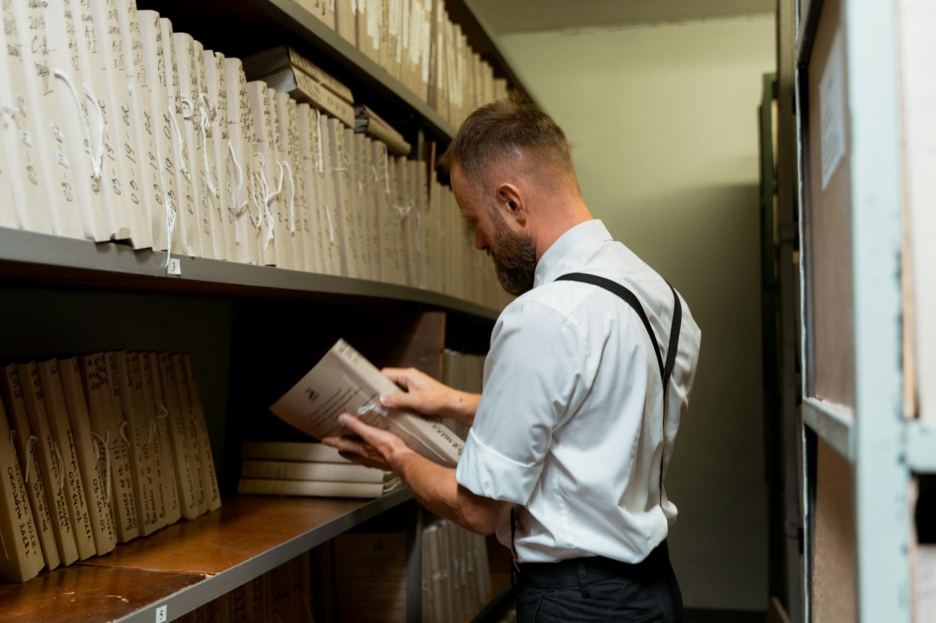 A man in smart casual attire organizing files on shelves in an archive.