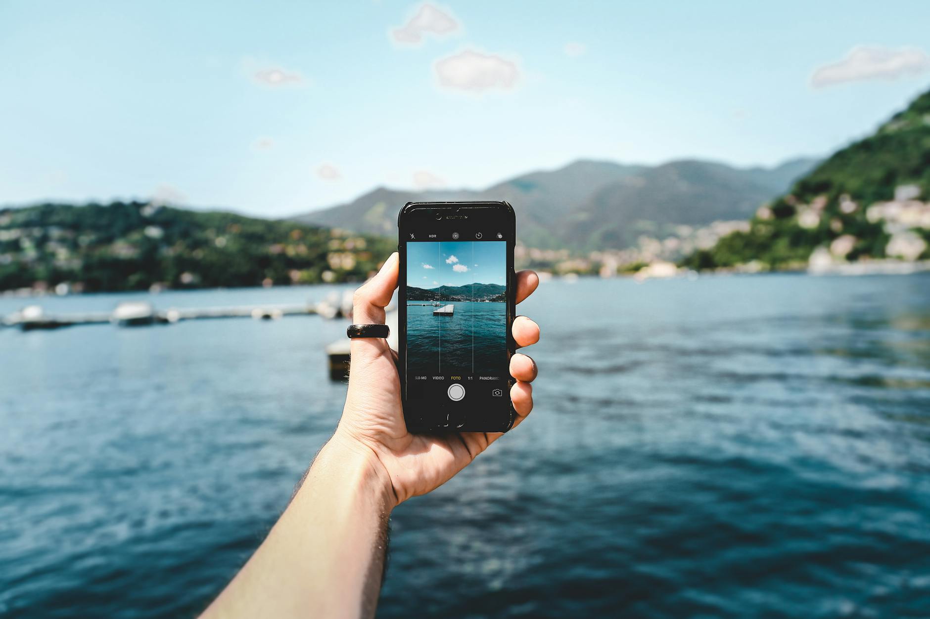 A person photographing a beautiful lake view using a smartphone, showcasing modern technology in nature.