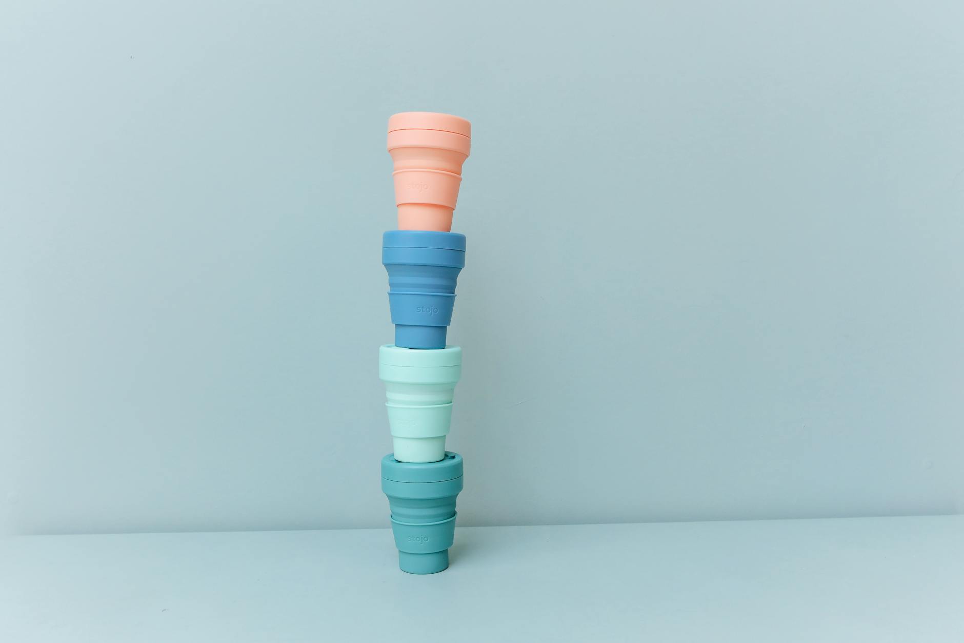 A set of colorful reusable cups stacked on a pastel blue background, symbolizing sustainability and zero waste.