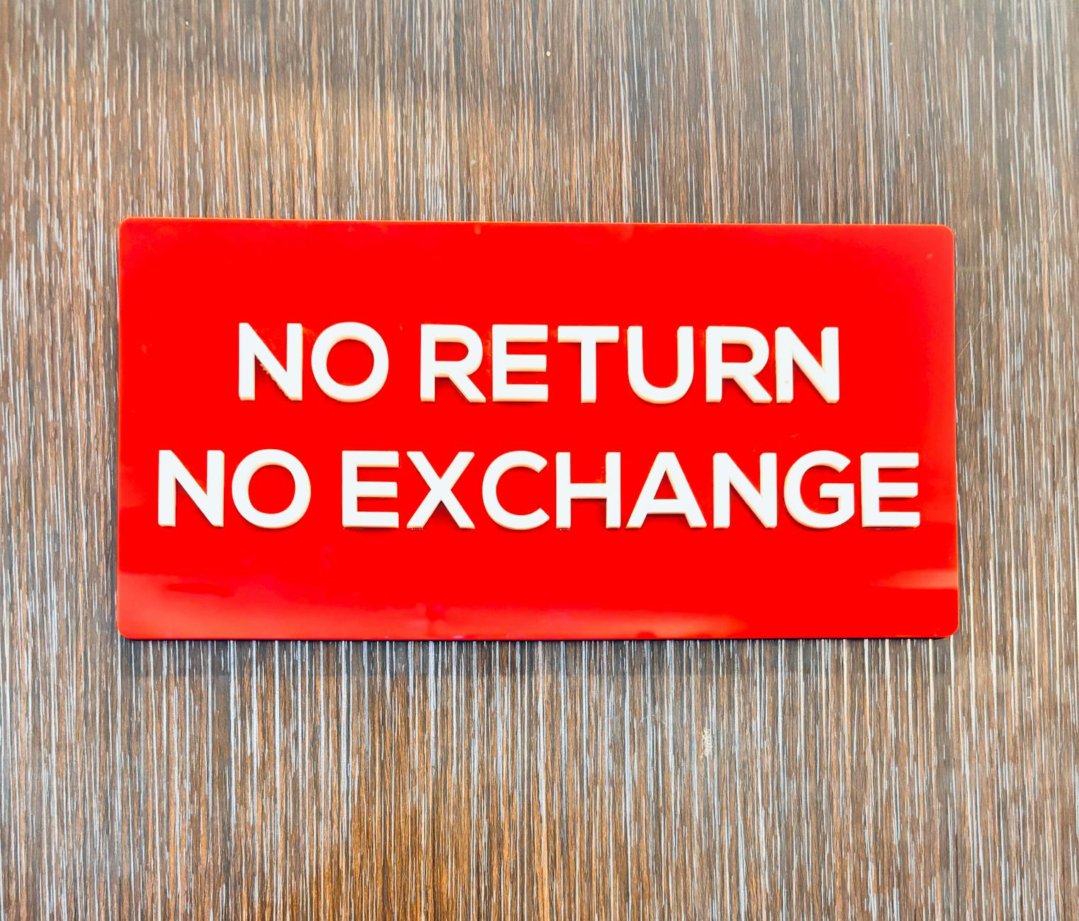 Bold red sign with 'No Return No Exchange' message on a wooden backdrop.