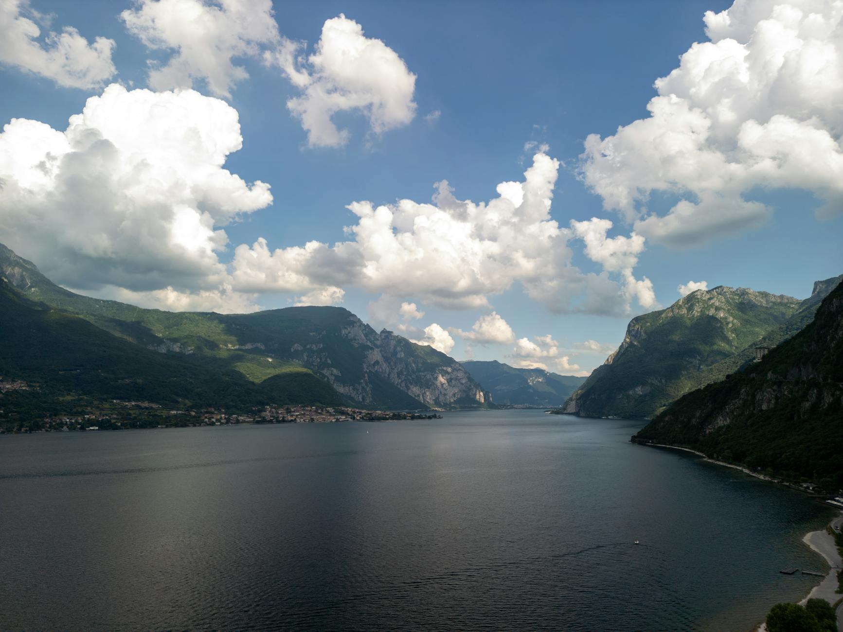 Breathtaking aerial view of Lake Como with lush mountains and fluffy clouds under a bright summer sky.