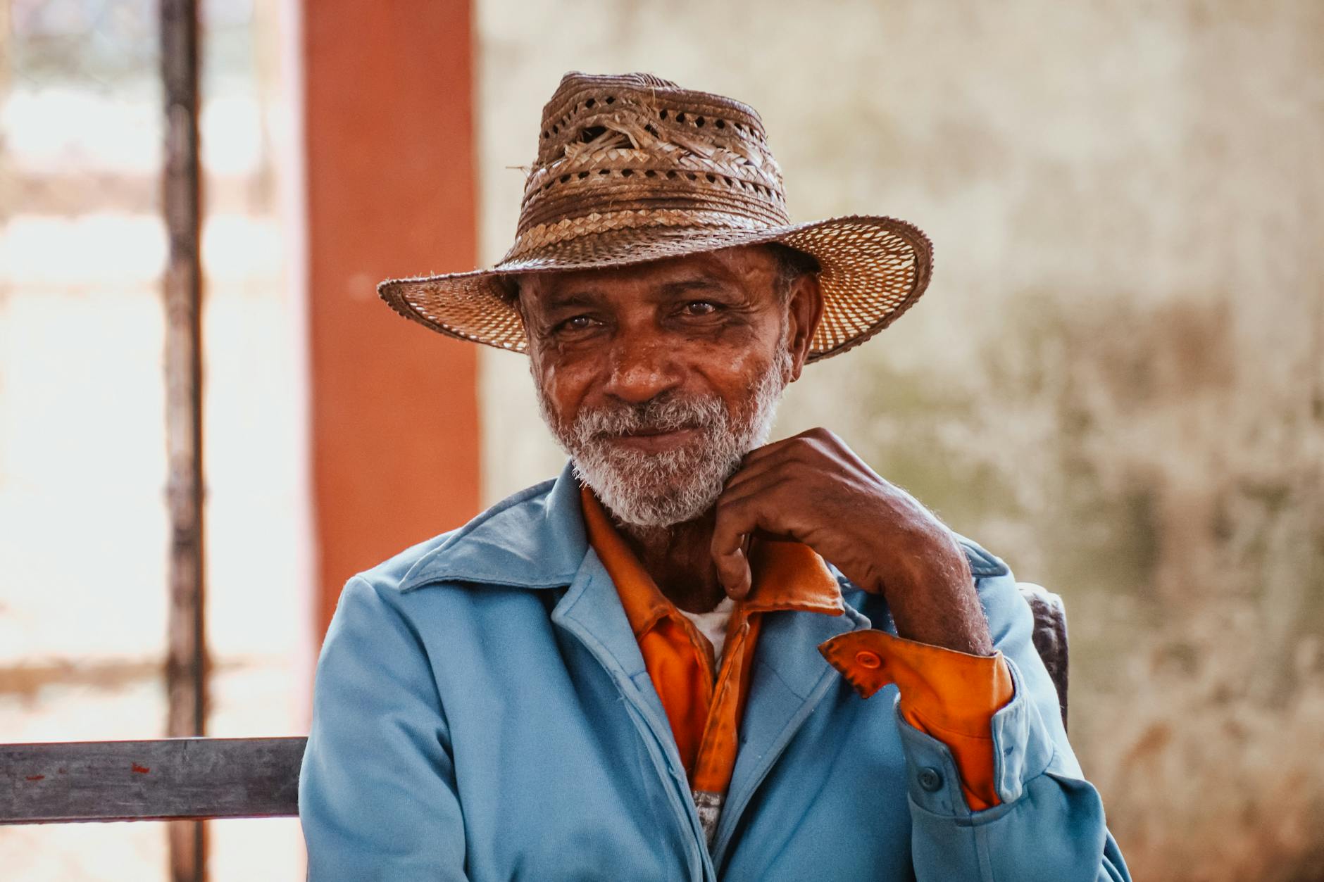Content mature Asian male in worn out straw hat touching chin and looking away while standing on sunny street