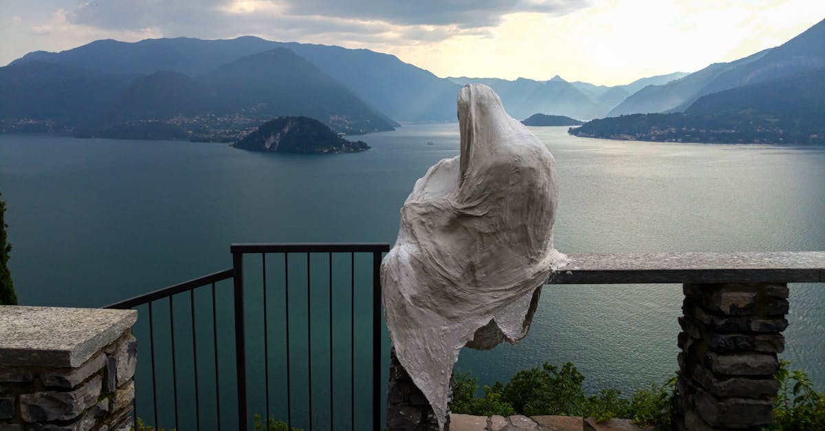 A mysterious sculpture gazes over Lake Como in Lombardia, Italy, surrounded by serene mountain views.