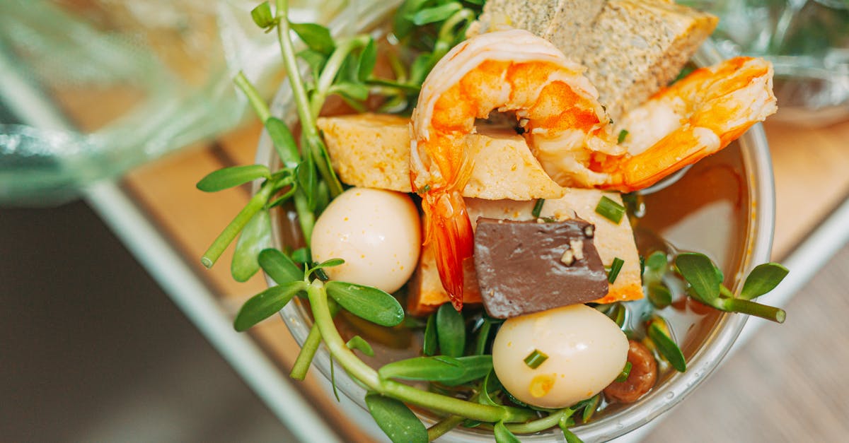 A vibrant overhead shot of Thai Tom Yum soup featuring shrimp, tofu, quail eggs, vegetables, and greens.
