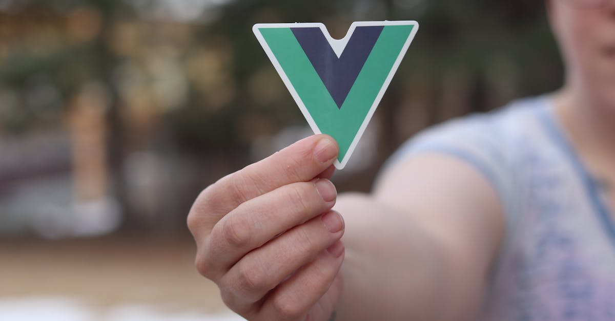 Close-up of a person holding a Vue.js logo sticker outdoors during springtime.
