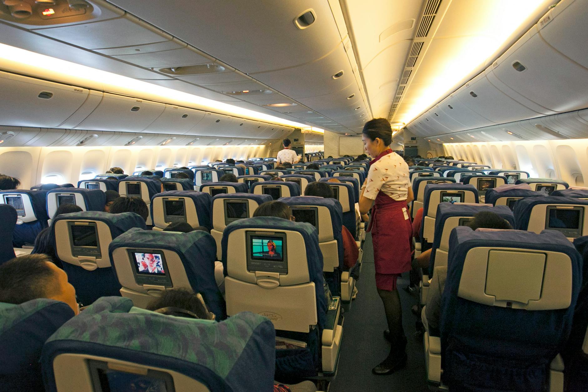 Flight attendant assisting passengers in a busy airplane cabin, ensuring a comfortable travel experience.