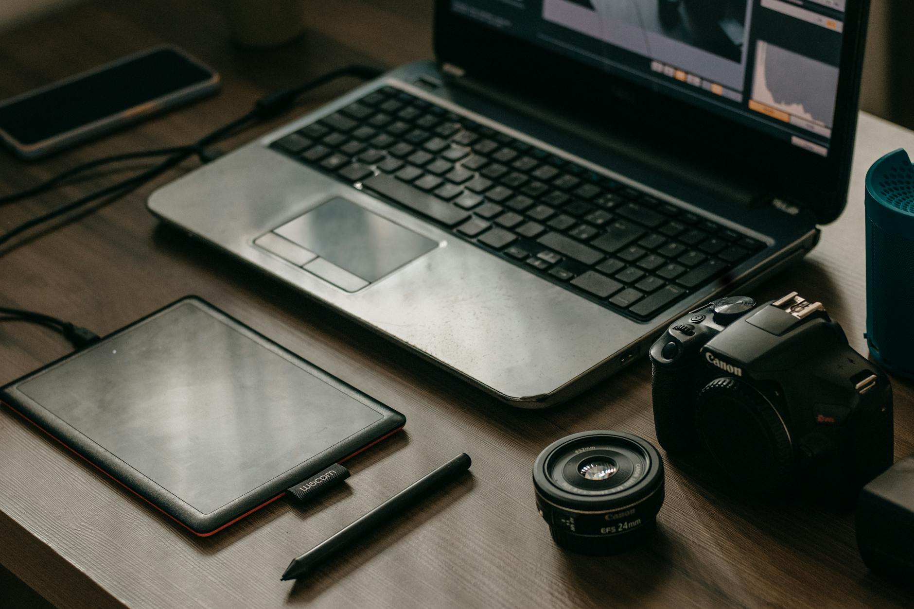 Laptop, camera, lens, and graphic tablet on a desk for digital creatives.