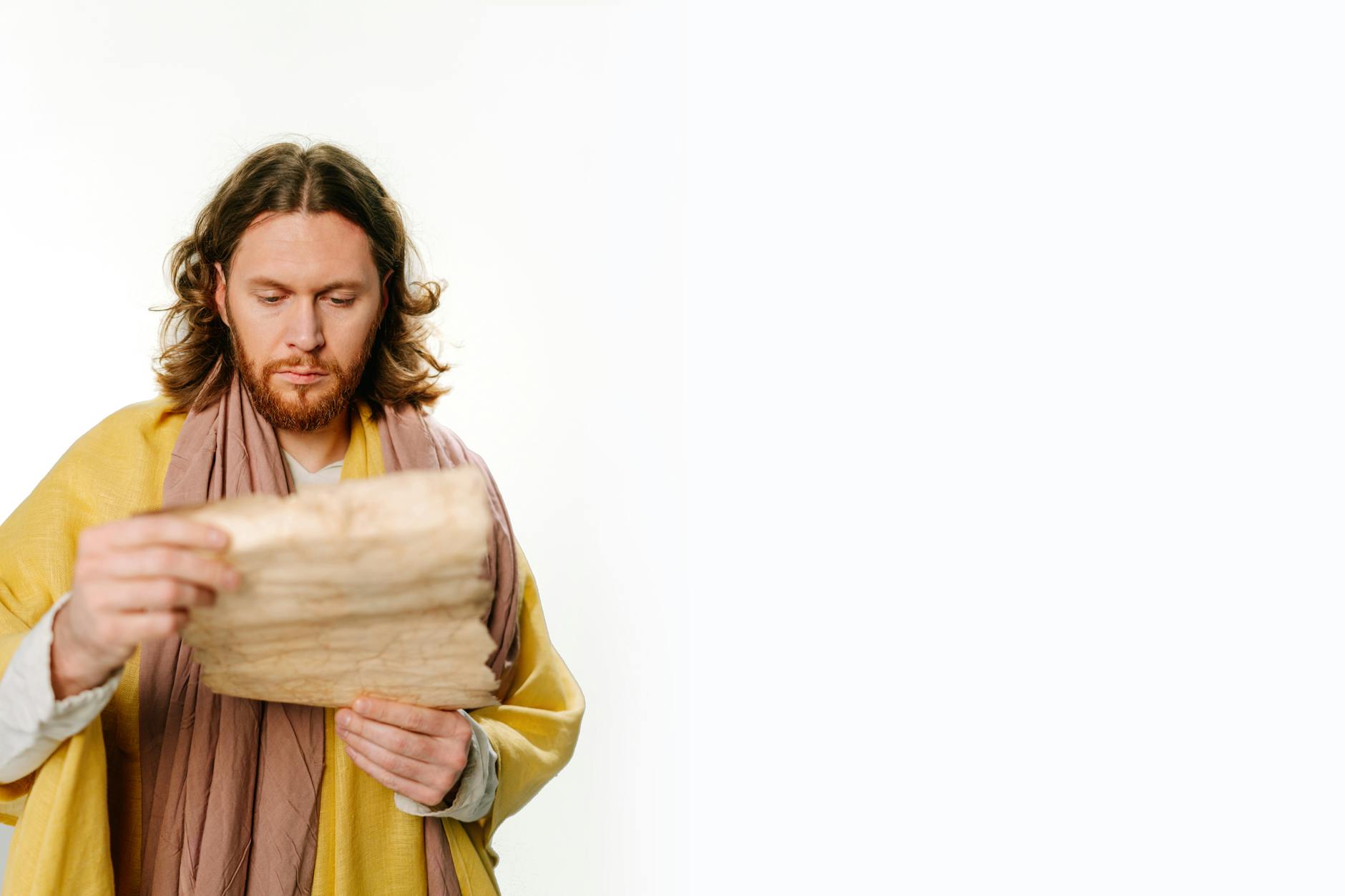 Man with long hair and beard reading an ancient scroll on a white background.