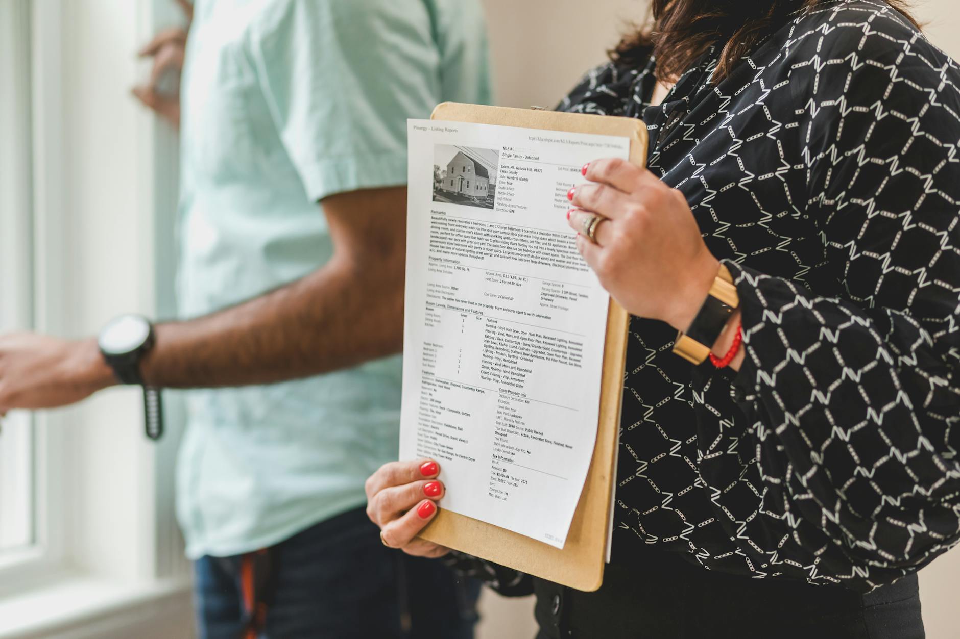 Real estate agent holding property documents on a clipboard in an office setting.