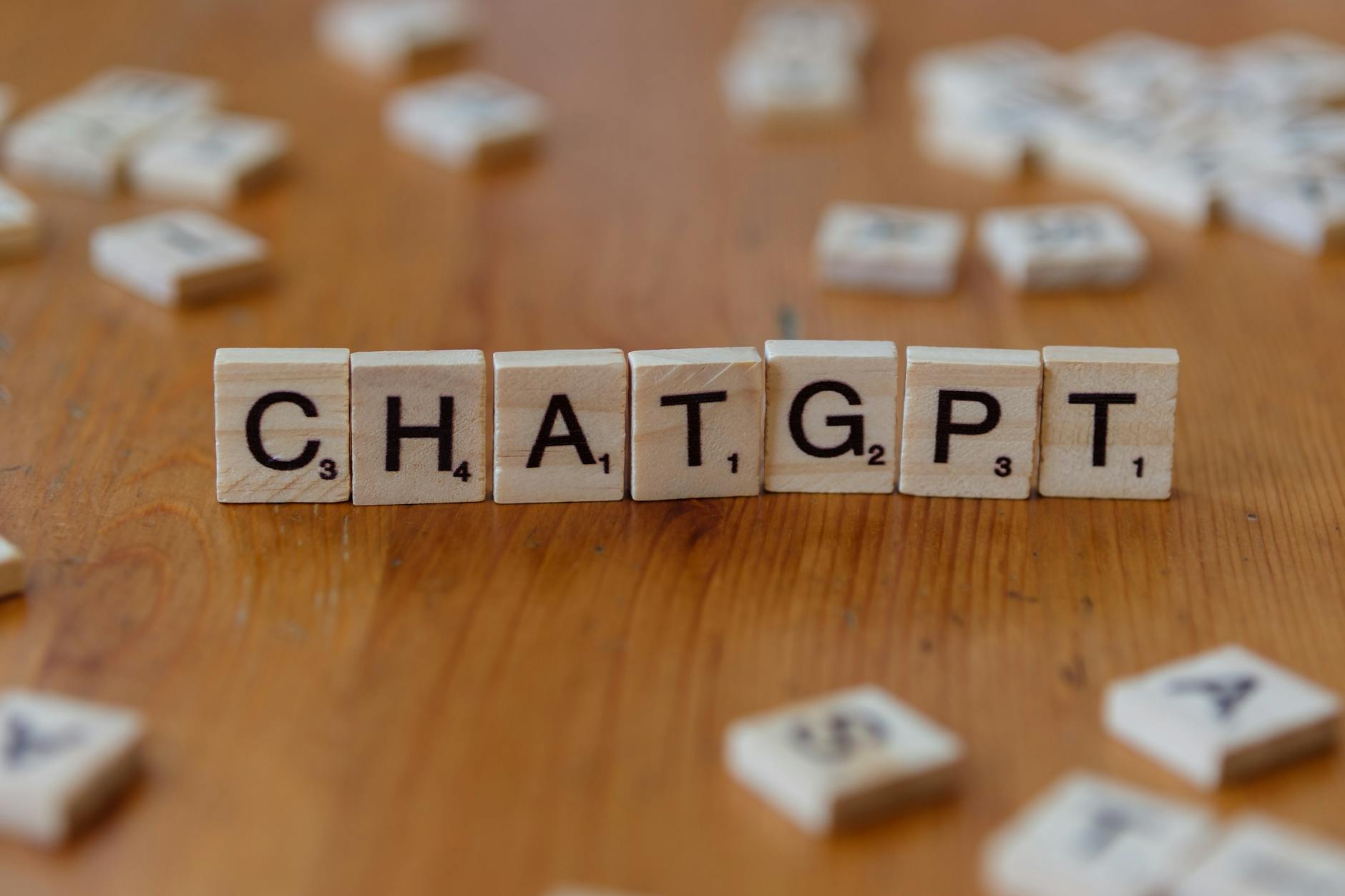 Scrabble tiles spelling "CHATGPT" on wooden surface, emphasizing AI language models.