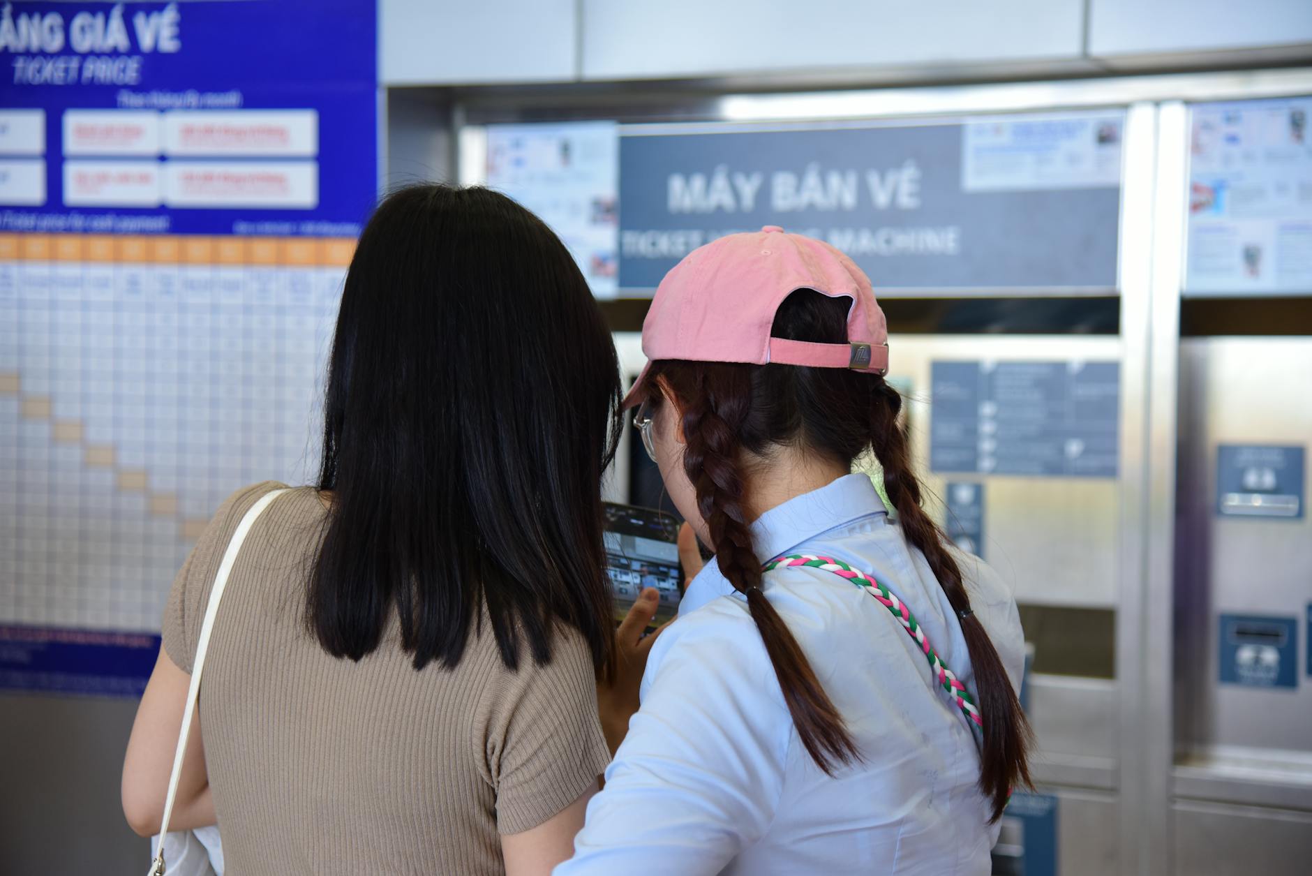 Two women purchasing tickets from a vending machine at a public transport station.