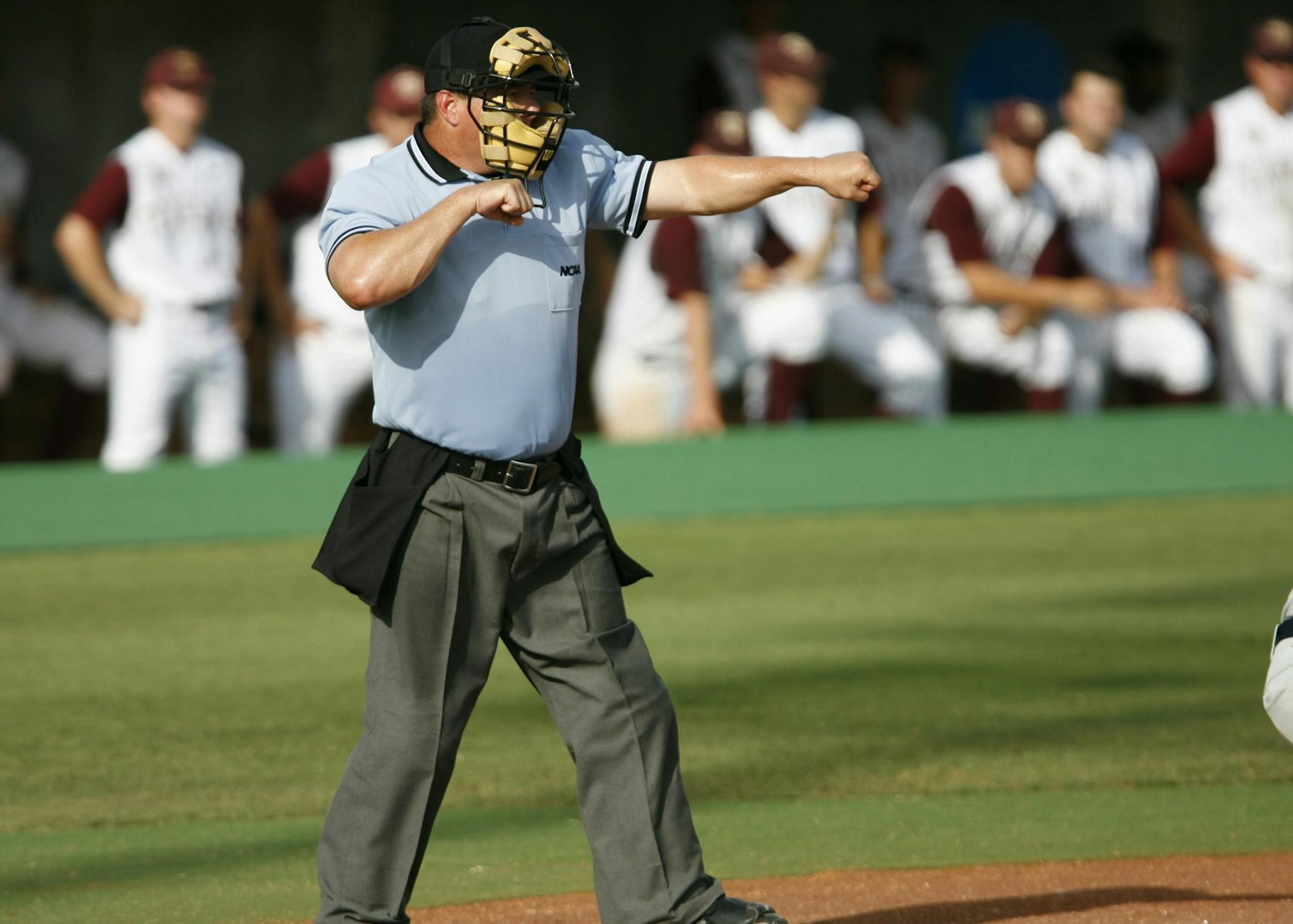 Umpire in action on baseball field with team players in the background.